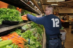 An employee at West Seattle Thriftway stocks produce. The store recently installed energy efficient LED lighting and made many other energy-saving changes.