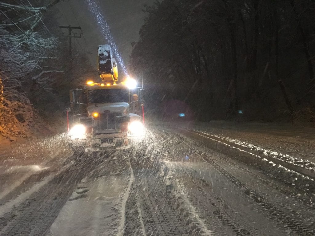 A Seattle City Light truck driving on a road covered in snow at night
