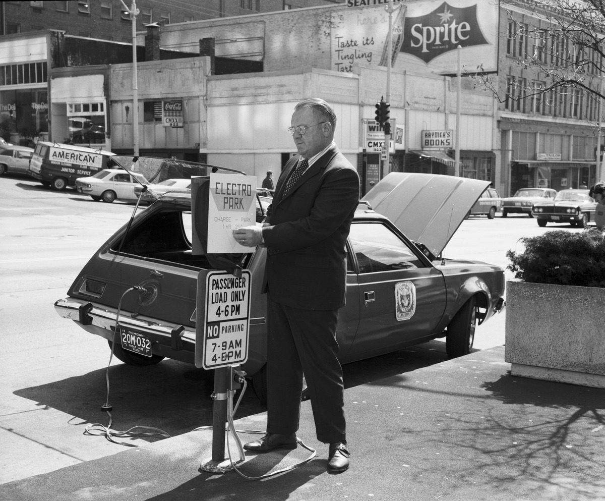 Man in suit charging a 1973 AMC Gremlin electric vehicle