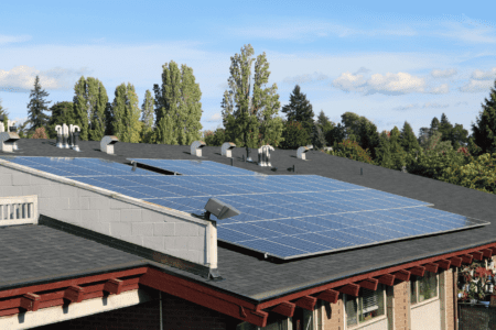 Installation of solar panels on a roof with trees in the background.