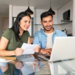 Smiling Latin American couple paying utility bills at home using their laptop