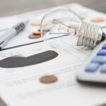 A light bulb, a pen, a calculator and some copper euro cent coins lie on top of an electricity bill.