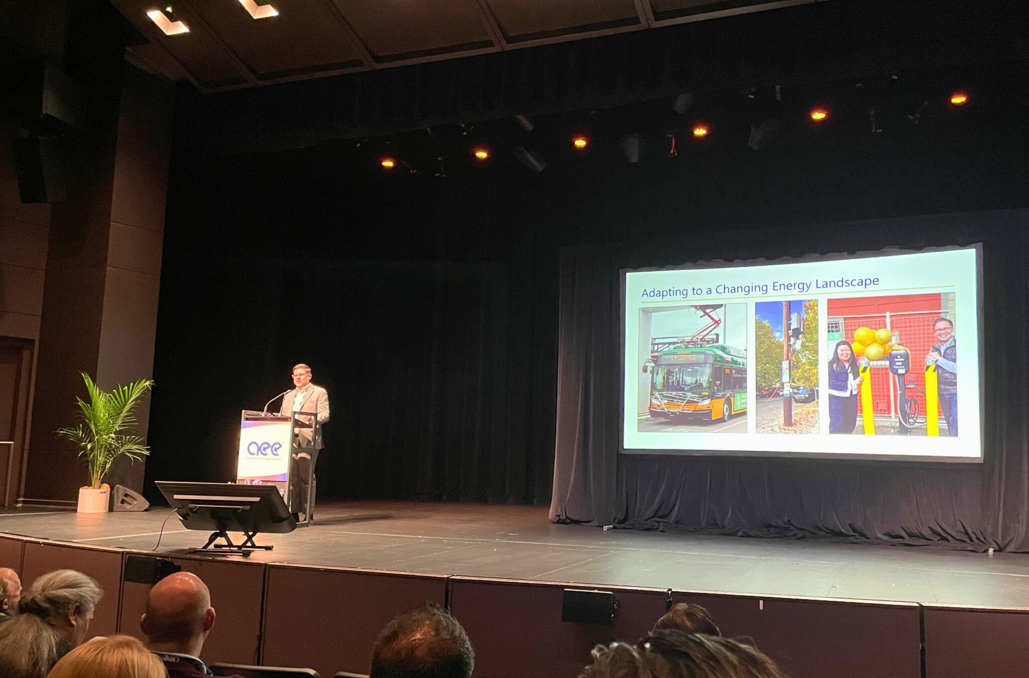 David Logsdon stands at a podium during a conference with a presentation slide showing a bus and energy-related images.